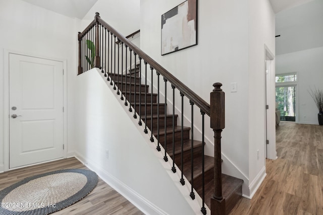 stairway with light hardwood / wood-style flooring and a towering ceiling