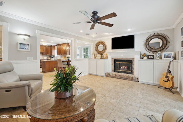 tiled living room featuring ceiling fan, crown molding, and a brick fireplace