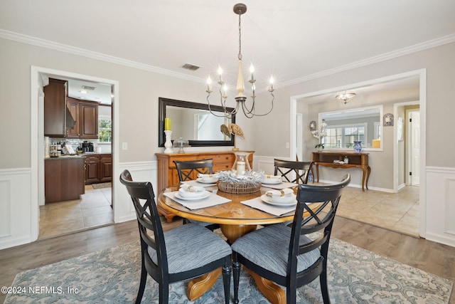 dining space with light hardwood / wood-style floors, crown molding, a wealth of natural light, and a chandelier