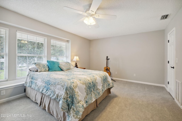 bedroom featuring a textured ceiling, light colored carpet, and ceiling fan