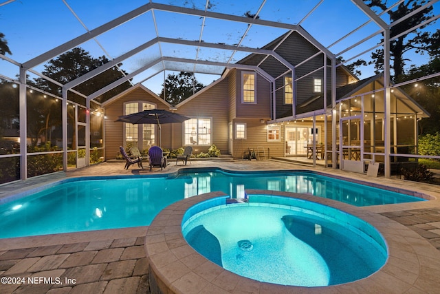 pool at dusk featuring an in ground hot tub, a patio area, and a lanai