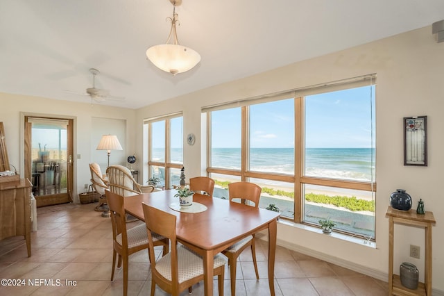 dining room with a water view, ceiling fan, a beach view, and light tile patterned floors