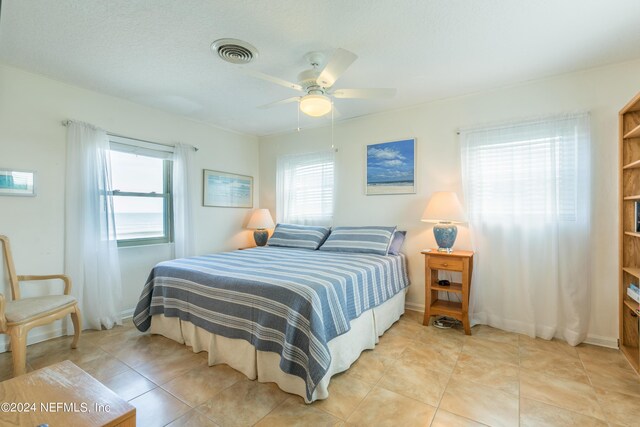 tiled bedroom featuring ceiling fan, multiple windows, and a textured ceiling