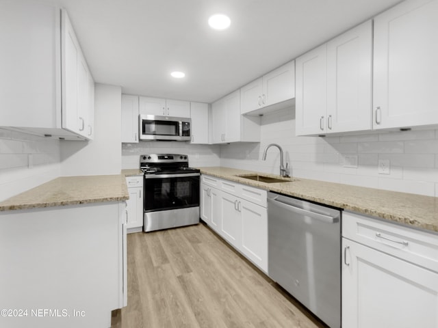 kitchen with tasteful backsplash, white cabinetry, sink, light hardwood / wood-style flooring, and stainless steel appliances