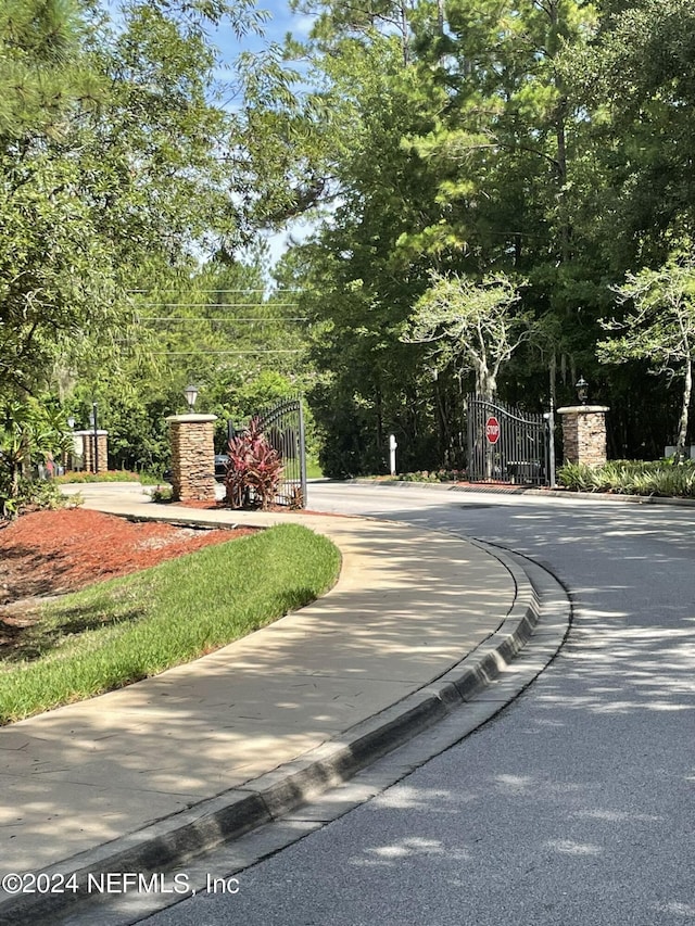 view of asphalt road with a gate, traffic signs, and curbs
