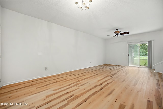 spare room with wood finished floors, ceiling fan, a chandelier, and baseboards