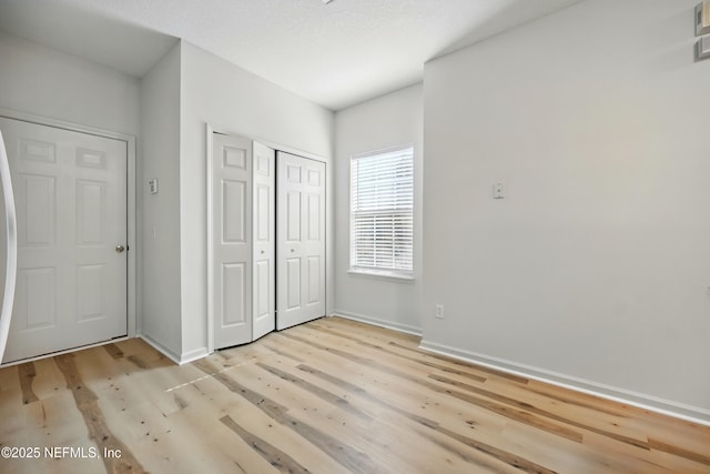unfurnished bedroom featuring light wood-style floors, baseboards, and a closet