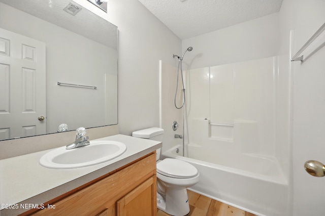 bathroom featuring wood finished floors, a textured ceiling, toilet, vanity, and tub / shower combination