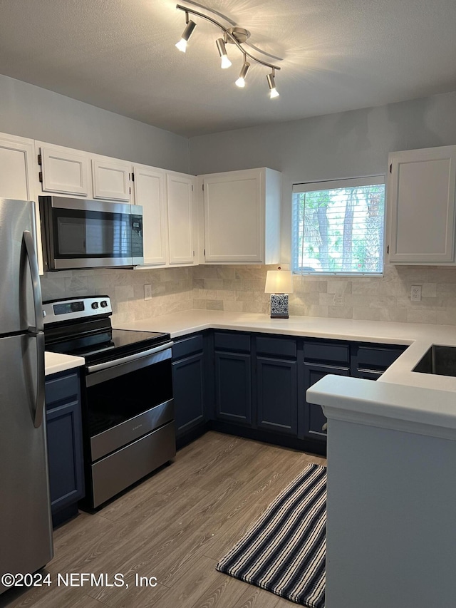 kitchen with a textured ceiling, light wood-type flooring, white cabinets, stainless steel appliances, and backsplash