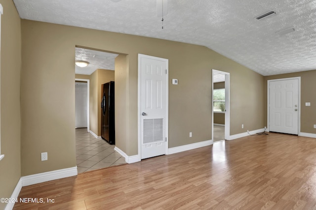 spare room featuring light hardwood / wood-style flooring, vaulted ceiling, and a textured ceiling