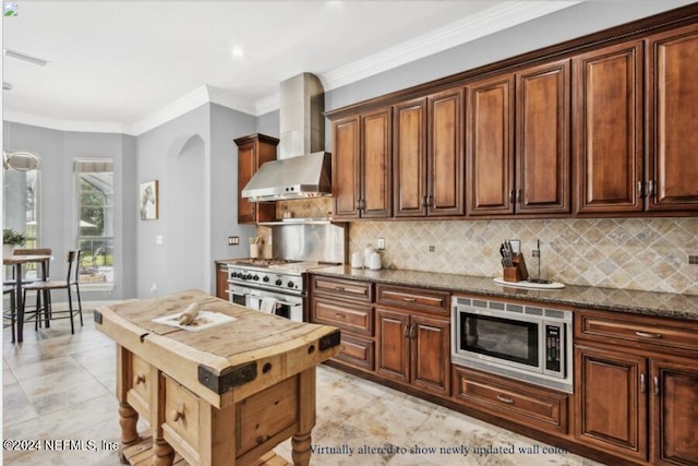 kitchen with wall chimney exhaust hood, crown molding, dark stone countertops, appliances with stainless steel finishes, and backsplash