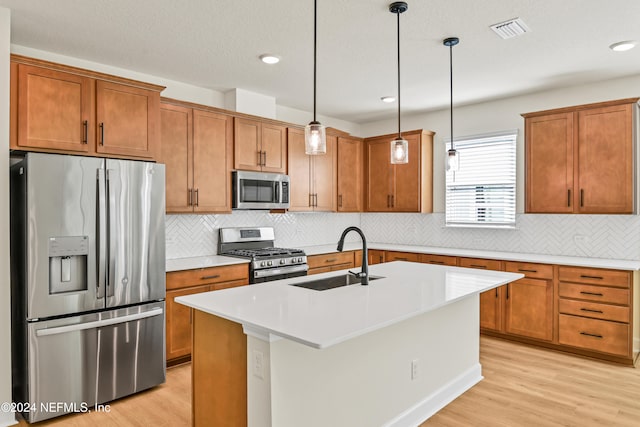 kitchen featuring sink, hanging light fixtures, appliances with stainless steel finishes, an island with sink, and light hardwood / wood-style floors