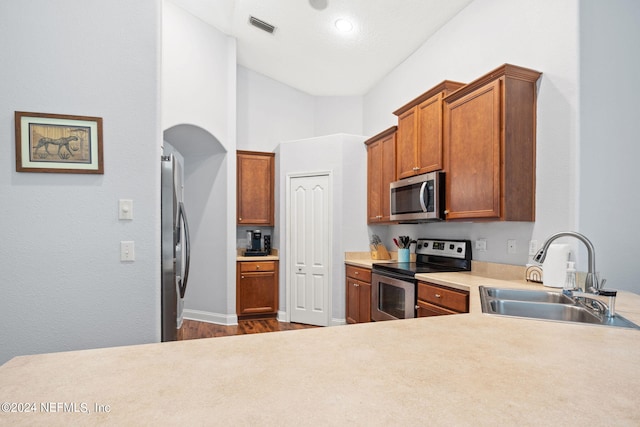 kitchen featuring hardwood / wood-style flooring, appliances with stainless steel finishes, sink, and a towering ceiling