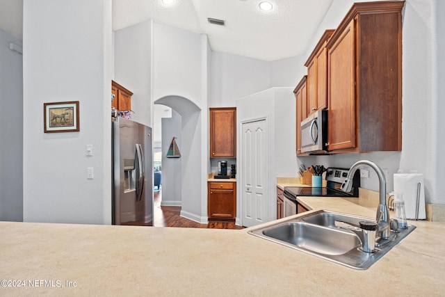 kitchen featuring sink, a textured ceiling, appliances with stainless steel finishes, hardwood / wood-style flooring, and a towering ceiling