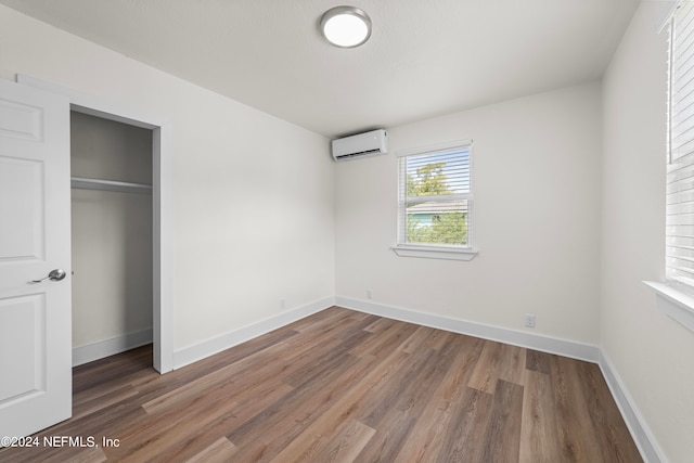 unfurnished bedroom with a closet, an AC wall unit, and hardwood / wood-style floors