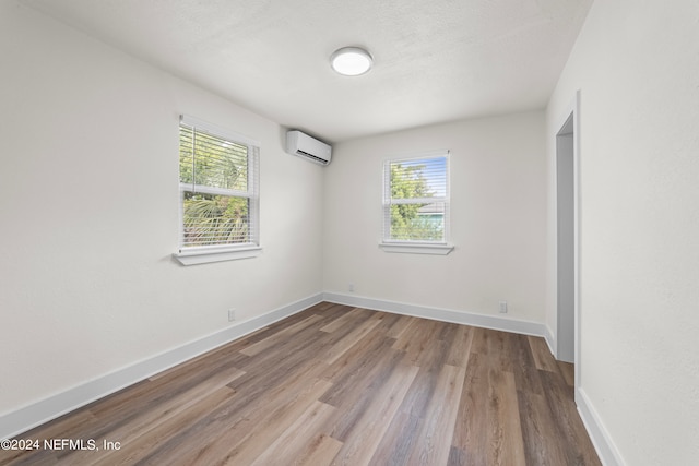 spare room featuring a wall mounted air conditioner, hardwood / wood-style floors, and plenty of natural light