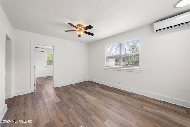 empty room with wood-type flooring, an AC wall unit, and ceiling fan