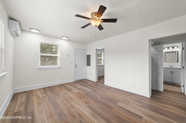 unfurnished bedroom with an AC wall unit, light hardwood / wood-style flooring, electric panel, ceiling fan, and ensuite bathroom