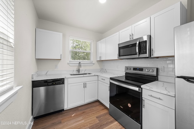 kitchen featuring appliances with stainless steel finishes, tasteful backsplash, white cabinets, hardwood / wood-style floors, and sink