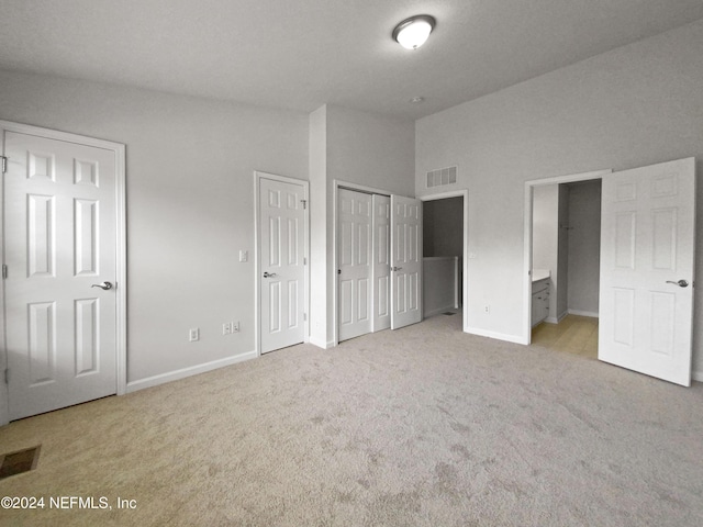 unfurnished bedroom with two closets, light colored carpet, and ensuite bath