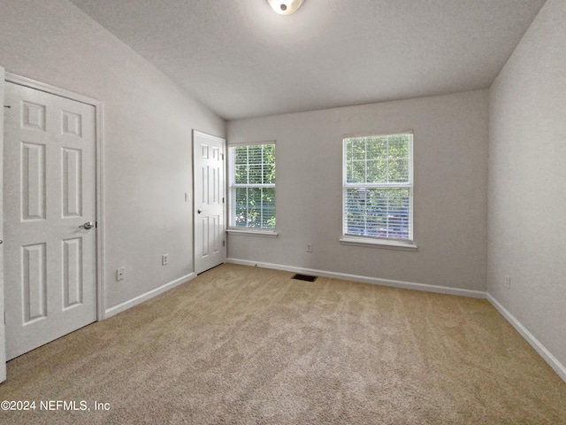 spare room featuring light colored carpet, lofted ceiling, and a textured ceiling