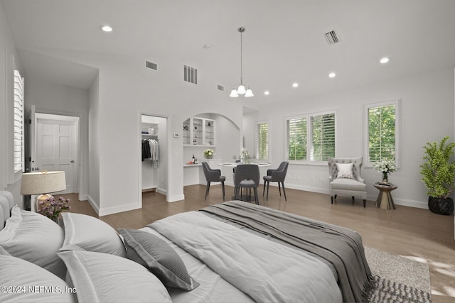 bedroom featuring a spacious closet, a closet, wood-type flooring, and an inviting chandelier