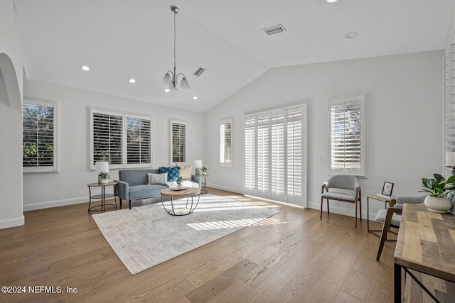 living room with a wealth of natural light, light hardwood / wood-style floors, vaulted ceiling, and a notable chandelier