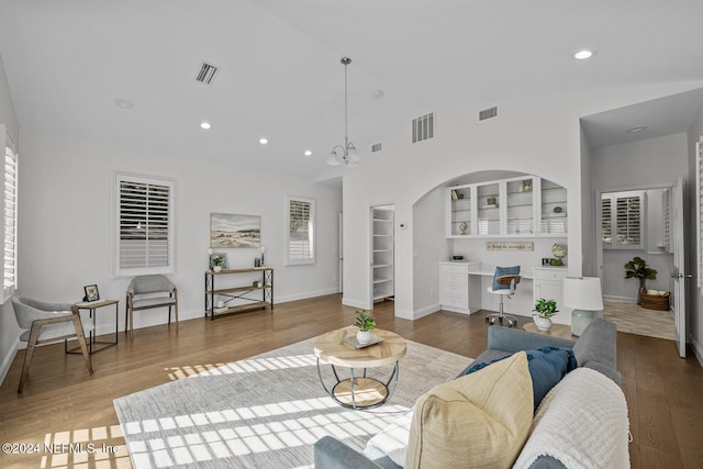 living room with hardwood / wood-style floors, built in shelves, built in desk, and an inviting chandelier