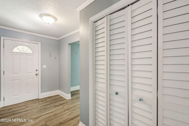 entryway featuring light wood-style floors, crown molding, a textured ceiling, and baseboards