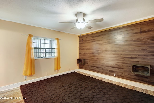 unfurnished room with a textured ceiling, ceiling fan, wooden walls, baseboards, and ornamental molding