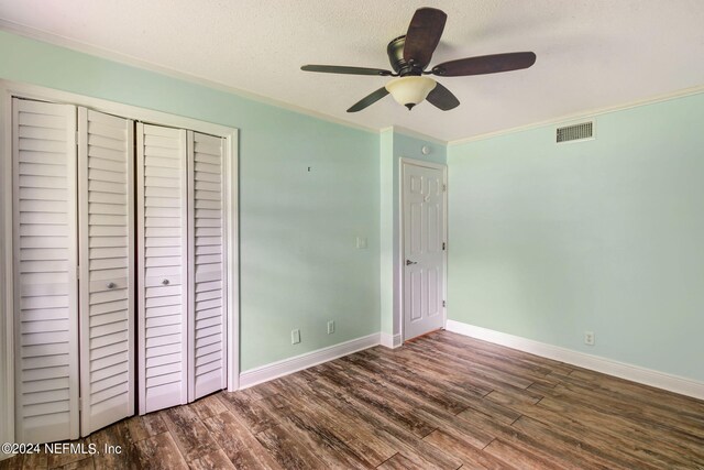 unfurnished bedroom featuring crown molding, a closet, visible vents, wood finished floors, and baseboards