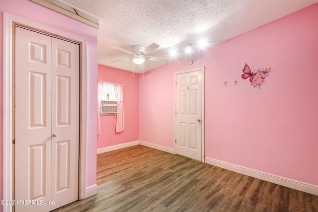 empty room featuring a textured ceiling, ceiling fan, cooling unit, wood finished floors, and baseboards