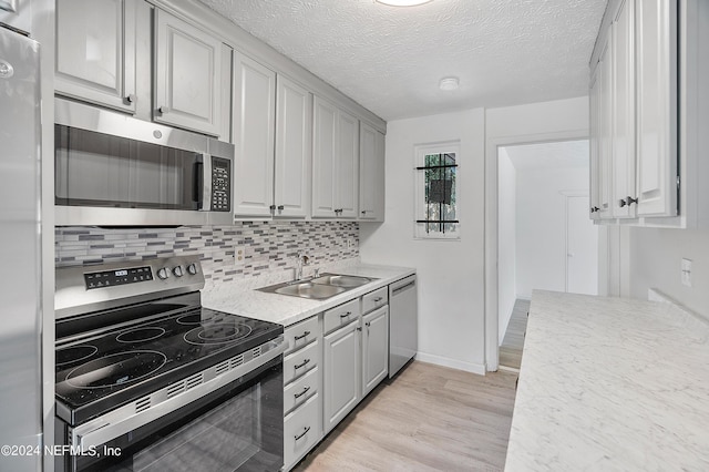 4435 Bedivere Rd, Jacksonville, FL 32208 - kitchen with tasteful backsplash, stainless steel appliances, a textured ceiling, a sink, and light wood-style flooring