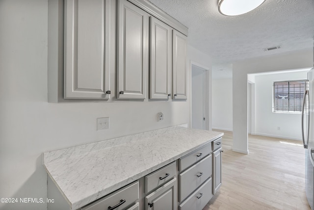 4435 Bedivere Rd, Jacksonville, FL 32208 - kitchen with gray cabinets, freestanding refrigerator, a textured ceiling, light wood-type flooring, and visible vents