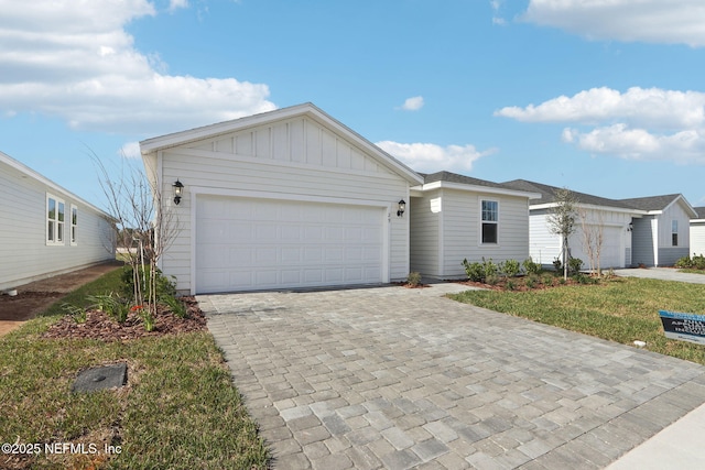 ranch-style home with decorative driveway, board and batten siding, an attached garage, and a front yard