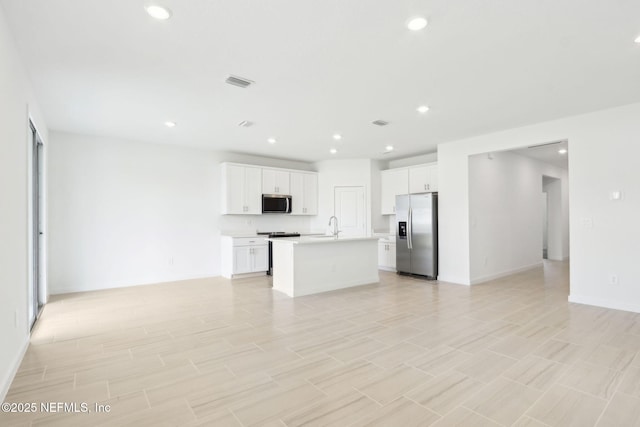 kitchen with a kitchen island with sink, stainless steel appliances, visible vents, open floor plan, and light countertops