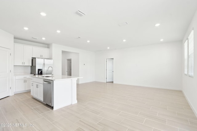 kitchen with stainless steel appliances, open floor plan, visible vents, and an island with sink