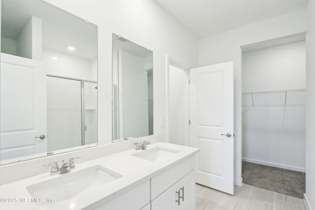 full bathroom with a spacious closet, double vanity, a stall shower, and a sink