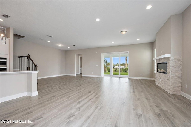 unfurnished living room with a stone fireplace and light wood-type flooring