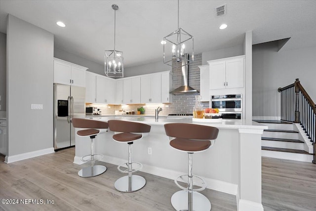 kitchen with white cabinetry, wall chimney range hood, a kitchen island with sink, and stainless steel appliances