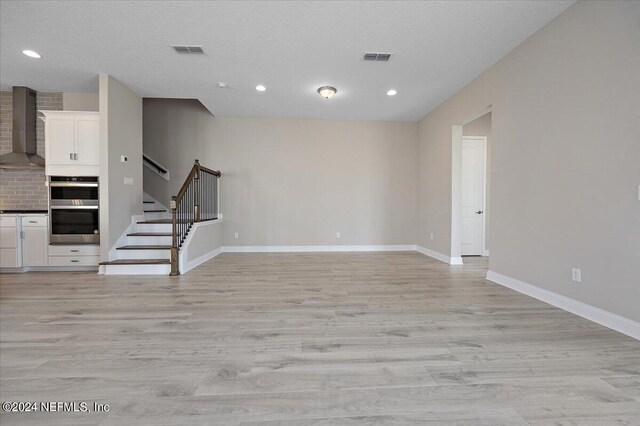 unfurnished living room with light wood-type flooring and a textured ceiling