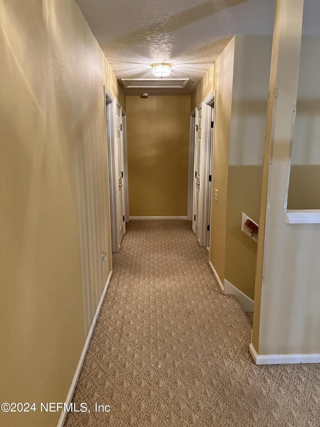 hallway with a textured ceiling, baseboards, and carpet flooring