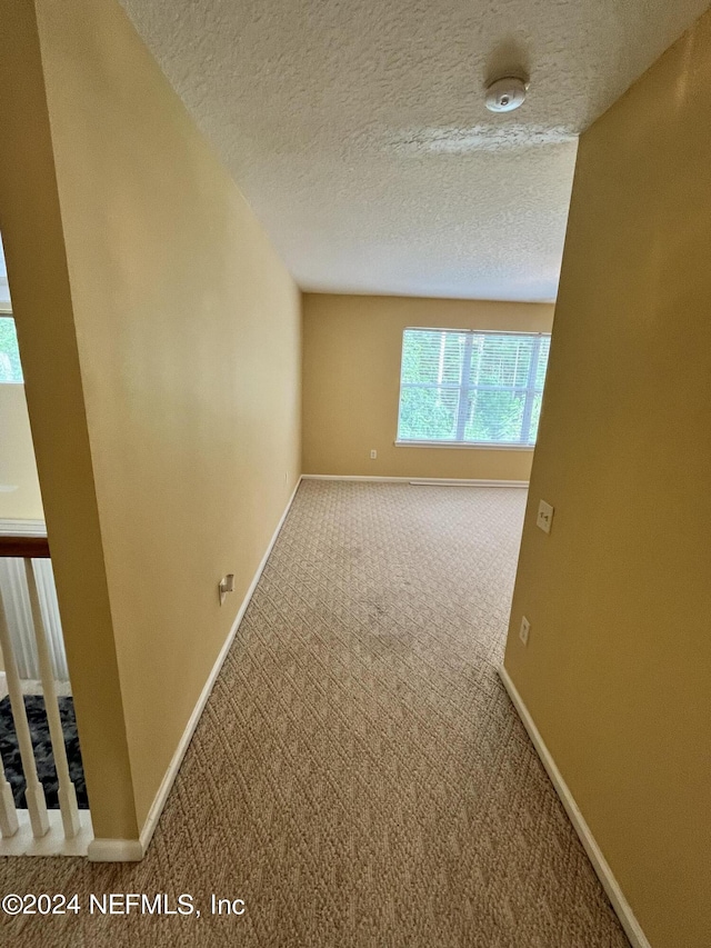 empty room featuring a textured ceiling, baseboards, and carpet flooring