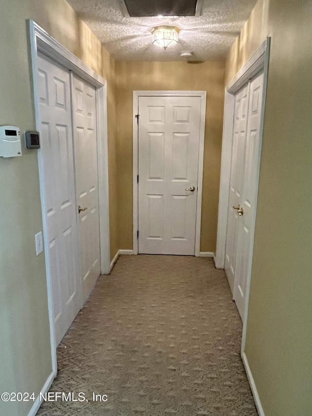 corridor with carpet flooring, a textured ceiling, and baseboards