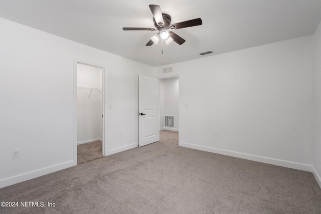 unfurnished bedroom featuring ceiling fan, light carpet, a closet, and a walk in closet