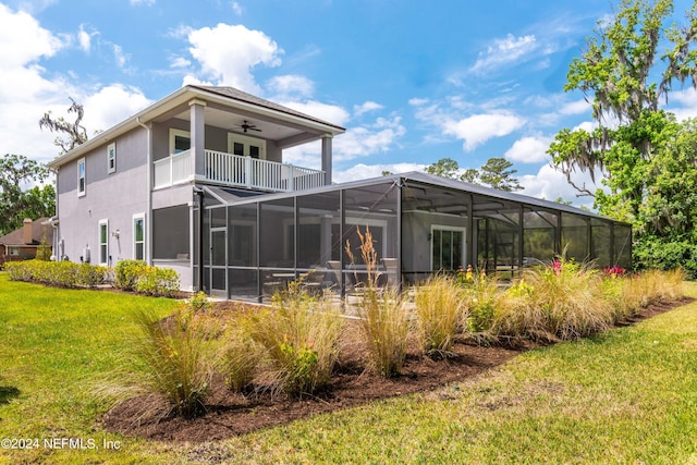 rear view of property with a balcony, glass enclosure, ceiling fan, and a lawn