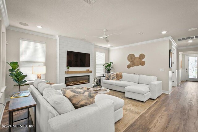 living room with ceiling fan, light wood-type flooring, crown molding, and a large fireplace