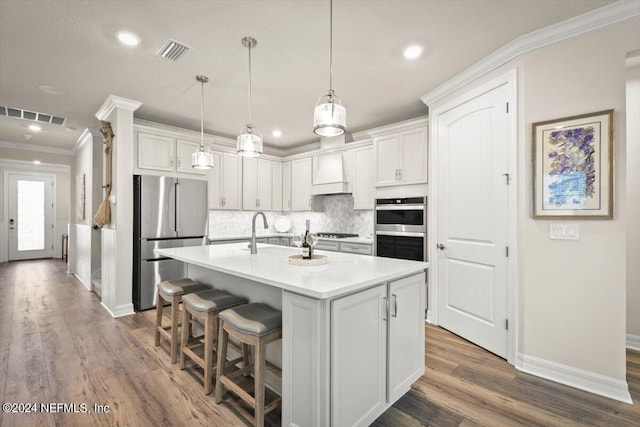 kitchen with white cabinets, a center island with sink, appliances with stainless steel finishes, and hanging light fixtures