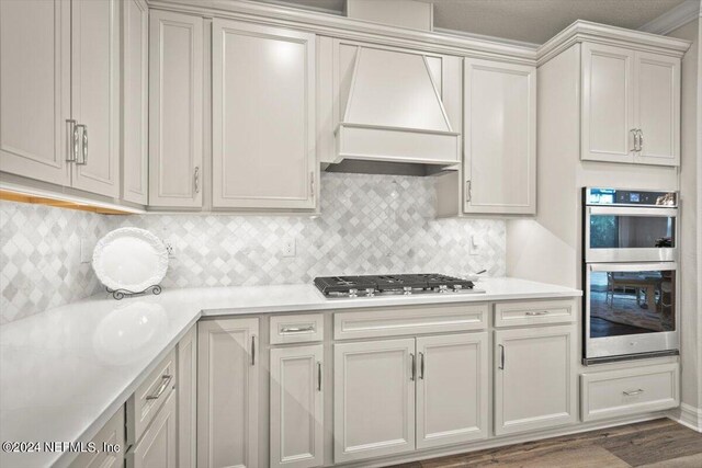 kitchen featuring ornamental molding, backsplash, dark wood-type flooring, appliances with stainless steel finishes, and custom range hood