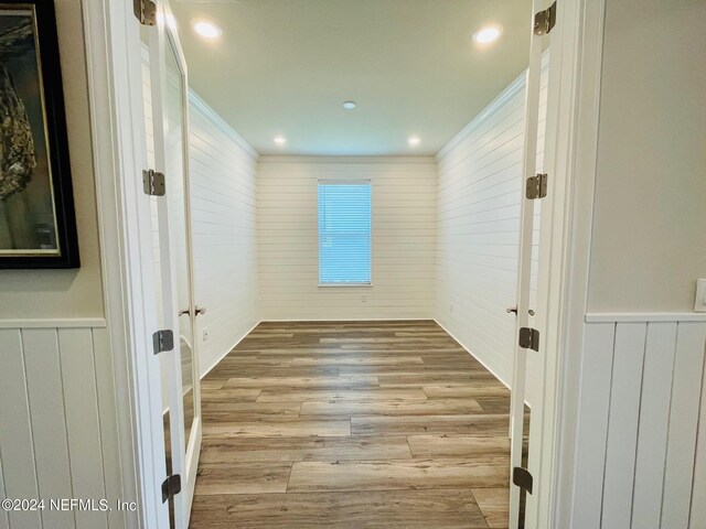 empty room featuring wood walls, ornamental molding, and light hardwood / wood-style flooring